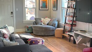 A living room with a grey sofa, a round ottoman, and a bookshelf with various items. - Rock House in Berkeley neighborhood of Denver (Denver)
