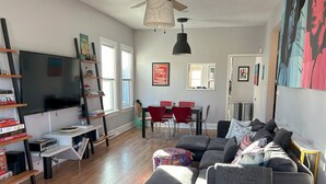 A modern living room with a sectional sofa, a flat-screen TV, and a dining area with red chairs. - Rock House in Berkeley neighborhood of Denver (Denver)