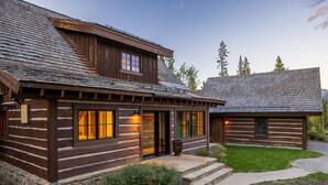 Una cabaña de troncos con cimientos de piedra, fachada de madera y césped bien cuidado.