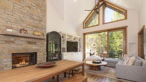 Un salón espacioso con chimenea de piedra, mesa de comedor de madera y un amplio ventanal con vistas al exterior.
