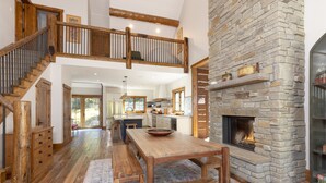 Una cocina amplia con chimenea de piedra, mesa de comedor de madera y un altillo con escalera de madera.