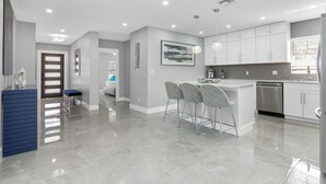 A modern kitchen with white cabinets, a stainless steel dishwasher, and a bar area with bar stools. - Sea Breeze Paradise - Walk to Vanderbilt Beach and Mercato, Heated Pool Home (Naples)
