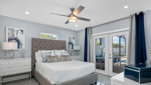 A modern bedroom with a large bed, a ceiling fan, and a view of the outdoor patio. - Sea Breeze Paradise - Walk to Vanderbilt Beach and Mercato, Heated Pool Home (Naples)