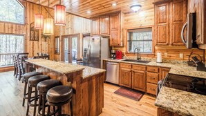 A wooden cabin kitchen with a bar area, wooden cabinets, and a large island. - Time Well Wasted- Spacious! Hot Tub,Shuffleboard,Playset,Free firewood! (Broken Bow)