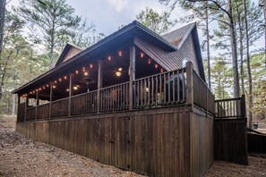 A wooden cabin with a balcony, string lights, and a metal roof. - Time Well Wasted- Spacious! Hot Tub,Shuffleboard,Playset,Free firewood! (Broken Bow)