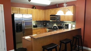 Una cocina moderna con electrodomésticos de acero inoxidable, armarios de madera, encimera de granito y taburetes de bar.