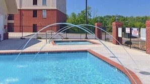 Una piscina con cerramiento de vidrio curvo, rodeada por un edificio de ladrillo y una valla de metal.