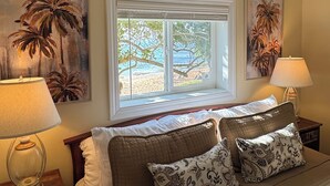 Ein Schlafzimmer mit einem Bett, zwei Nachttischen, einem Deckenventilator und einem Fenster mit Blick auf den Strand.