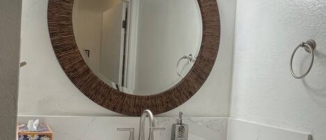 Een badkamer met een ronde spiegel, een wastafel en een houten opbergmeubel.
