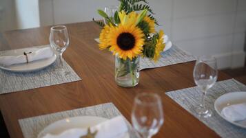 Una mesa de comedor dispuesta con platos blancos, servilletas y copas de vino, junto con un jarrón de girasoles y follaje verde.