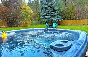 A hot tub with a duck, surrounded by a wooden fence, trees, and a grassy yard.