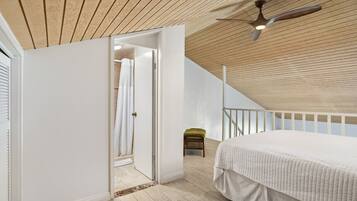 Une chambre avec un plafond en bois, un lit, un ventilateur de plafond et un escalier menant à un niveau supérieur.