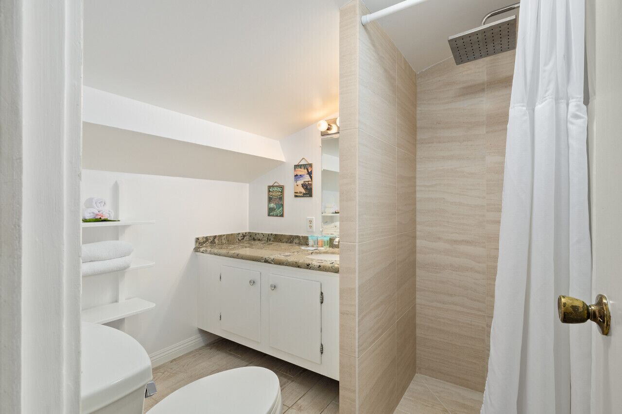 Ein Badezimmer mit Toilette, einem Waschbecken mit Granitablage, einer Dusche mit beige gefliestem Wand und einer weißen Tür mit Messinggriff.