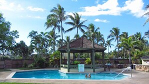 Ein Swimmingpool mit Pavillon, umgeben von Palmen und blauem Himmel.