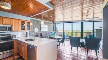 A modern kitchen with wooden cabinets, a large island, and a dining area with chairs and a table.