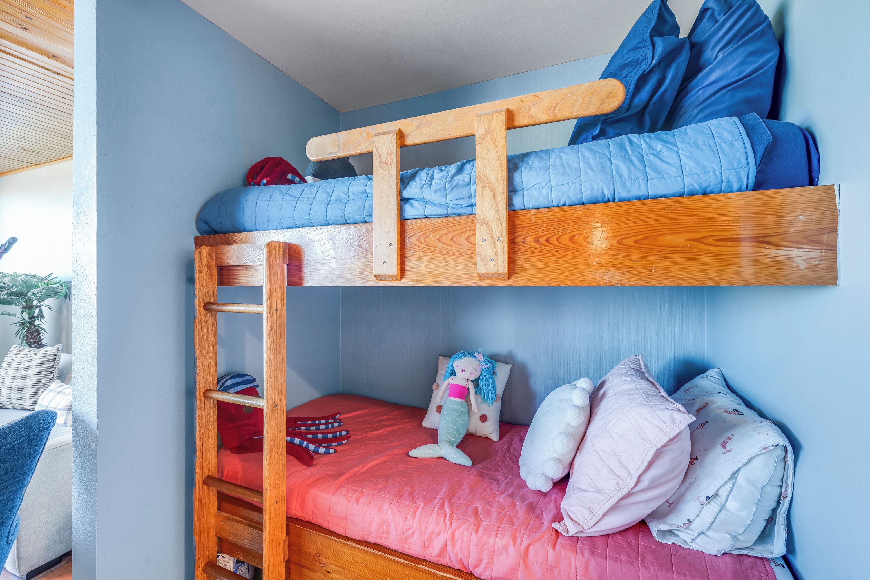 Ein Stockbett mit einer Holzleiter, einer roten Matratze und einer blauen gesteppten Matratze.