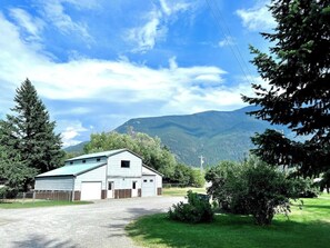 A single-story building with a garage, surrounded by a grassy area and trees, with mountains in the background.