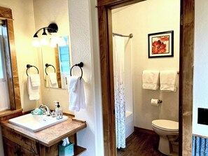 A bathroom with a sink, mirror, towel rack, shower curtain, toilet, and a framed picture on the wall.