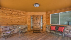 Eine Holzhütte mit einer Holztür, einer Bank mit roten Kissen und einem Tisch mit Stühlen.