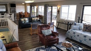 Un amplio salón con sofá, sillón y mesa de centro, un comedor con sillas y una cocina al fondo.