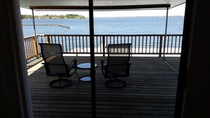 Una terraza de madera con dos sillas y una pequeña mesa, con vistas a una masa de agua y una costa distante.