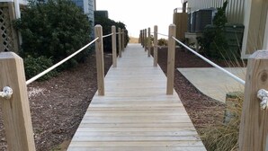 A wooden boardwalk leading to a building, surrounded by mulch and plants.
