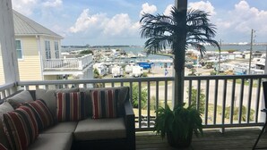 A balcony with a sofa and a palm tree, overlooking a marina with boats and a bridge.