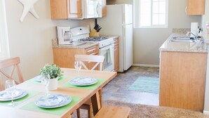 A spacious kitchen with wooden cabinets, a central island, and a dining area with a table set for four. - Beautiful & Clean!  White Water Views! (Oceanside)