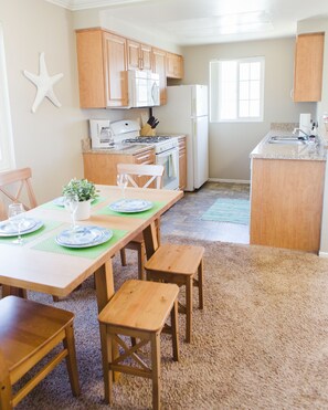 A spacious kitchen with wooden cabinets, a central island, and a dining area with a table set for four. - Beautiful & Clean!  White Water Views! (Oceanside)