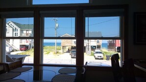 Habitación con un amplio ventanal que da a una playa y edificios. En primer plano, se observa una mesa con sillas.