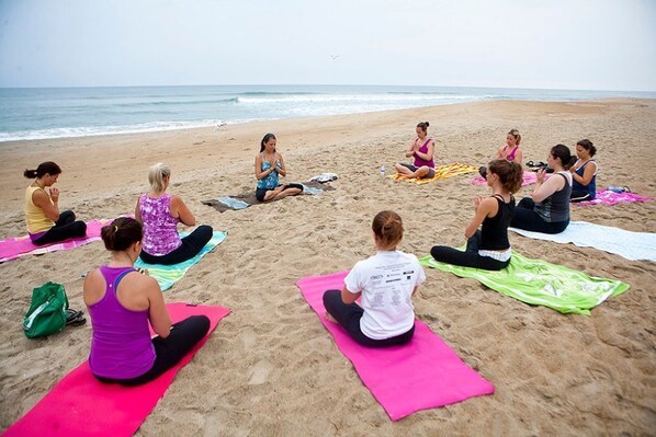 A group of people sitting on yoga mats on a beach, with the ocean in the background.