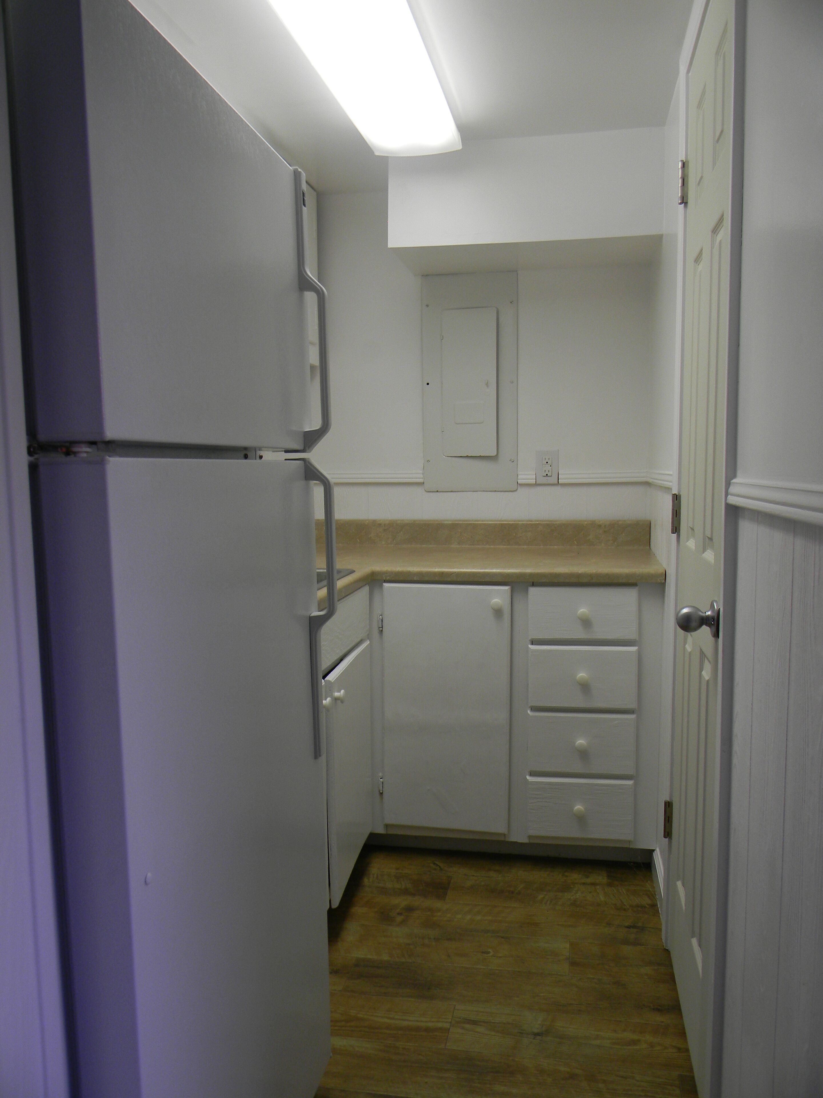 Une cuisine étroite avec des meubles blancs, un plan de travail en bois et une porte donnant sur une autre pièce.