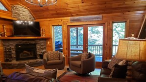 A cozy cabin interior with a stone fireplace, two armchairs, a leather sofa, and a wooden table.