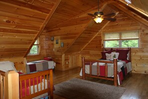 Une cabane chaleureuse avec une chambre à coucher située en mezzanine, un plafond en bois et une grande fenêtre.
