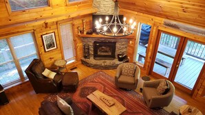 A cozy log cabin interior with a fireplace, leather sofas, and a chandelier.