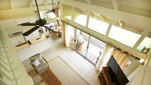 Un vaste espace de vie comprenant une table à manger, un canapé et un téléviseur. On y trouve également un ventilateur de plafond, de grandes fenêtres et une vue sur l’extérieur.