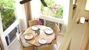 Un coin repas avec une table ronde dressée pour quatre personnes, entourée de chaises en osier.