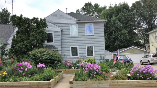 A two-story house with a garden in the front yard, featuring raised flower beds and various plants. - 2 bedroom, 1 bath apartment . Walk to Mayo, trails, parks, shopping, restaurants (Rochester)