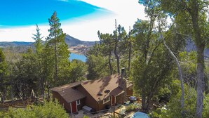 A single-story house with a stone chimney, surrounded by dense forest and a lake in the background. - PREMIUM TREE HOUSE  1.14-Acres  Hot Tub  Panoramic Lake Forest Mountain View (Julian)