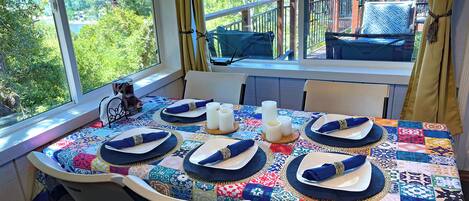 A dining table set for six with a colorful tablecloth, white candles, and blue napkins.