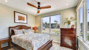 Une chambre avec un grand lit, un ventilateur de plafond, une commode, une fenêtre donnant sur l’extérieur et un tableau encadré accroché au mur.