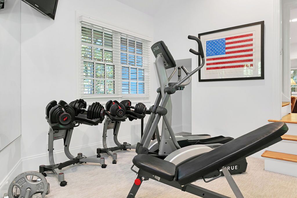 Ein Fitnessraum mit Krafttrainingsgeräten, einer Bank und einer gerahmten US-amerikanischen Flagge.
