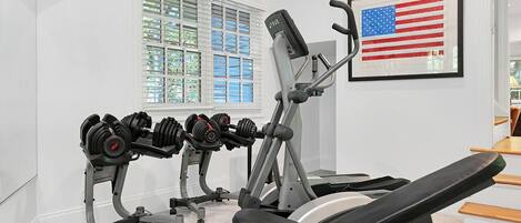 Ein Fitnessraum mit Krafttrainingsgeräten, einer Bank und einer gerahmten US-amerikanischen Flagge.