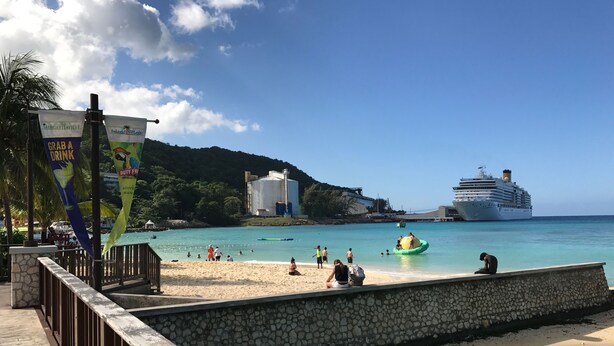 A beach with a wooden walkway, a large cruise ship, and a water slide. - Gordon's Beachfront Condo (Ocho Rios)