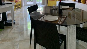 A dining area with a glass table, black chairs, a ceiling fan, and a view through the glass door. - Gordon's Beachfront Condo (Ocho Rios)