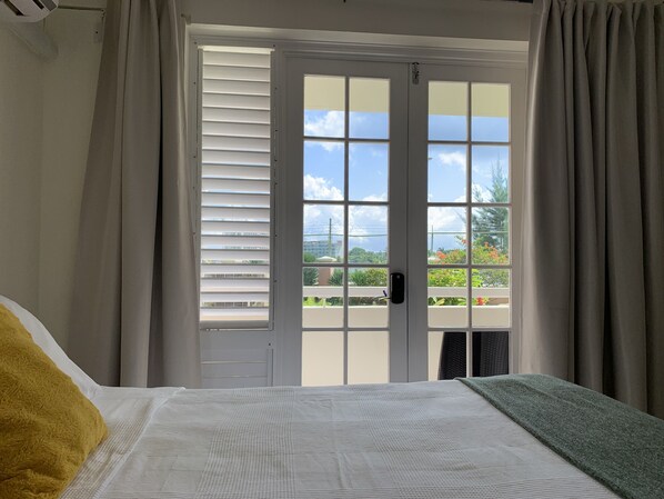 A bedroom with a bed, a window with blinds, and a view of the outdoors.