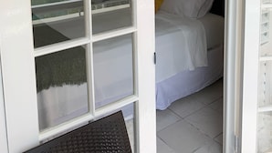 A bedroom with a bed, a wall-mounted air conditioning unit, and a window with a view of the sky and clouds. - Gordon's Beachfront Condo (Ocho Rios)