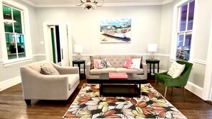 Un salon comprenant un canapé, deux fauteuils, une table basse, un tapis à motifs floraux, un lustre et un tableau accroché au mur.