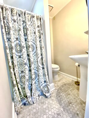 Un baño con cortina de ducha estampada, inodoro y lavamanos con piso de azulejos hexagonales.