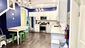 Une cuisine moderne avec des meubles blancs, des appareils en acier inoxydable et une table à manger en bois, accompagnée de tabourets verts.
